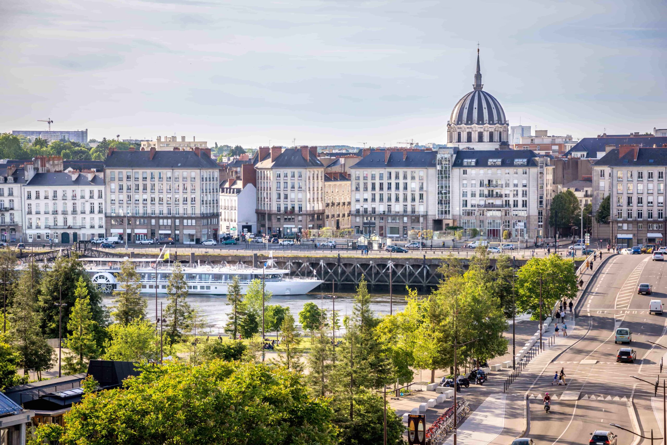 Vue panoramique sur les quais de la Loire à Nantes avec des immeubles haussmanniens et la basilique Saint-Nicolas en arrière-plan.