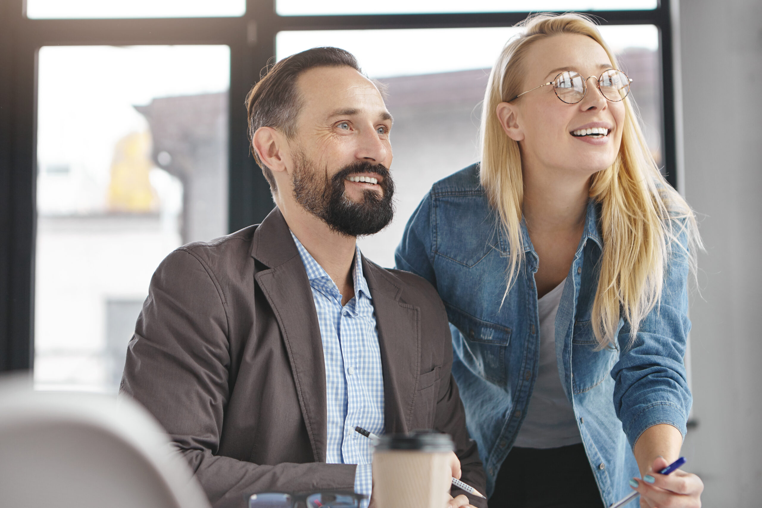Deux collègues souriants collaborent dans un bureau lumineux.
