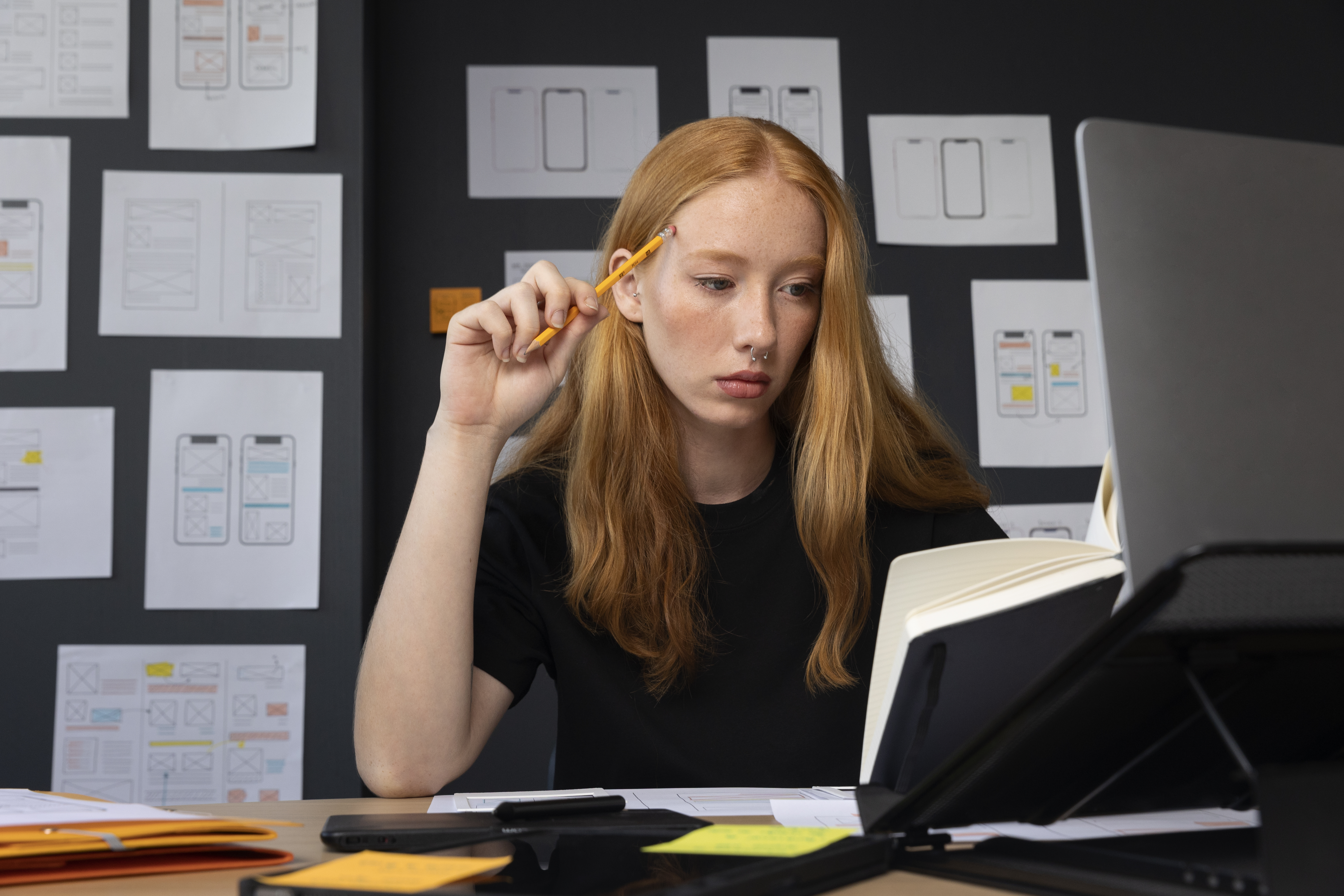 Jeune femme concentrée travaillant sur un projet de design UX/UI dans un bureau, entourée de croquis d’interfaces mobiles.