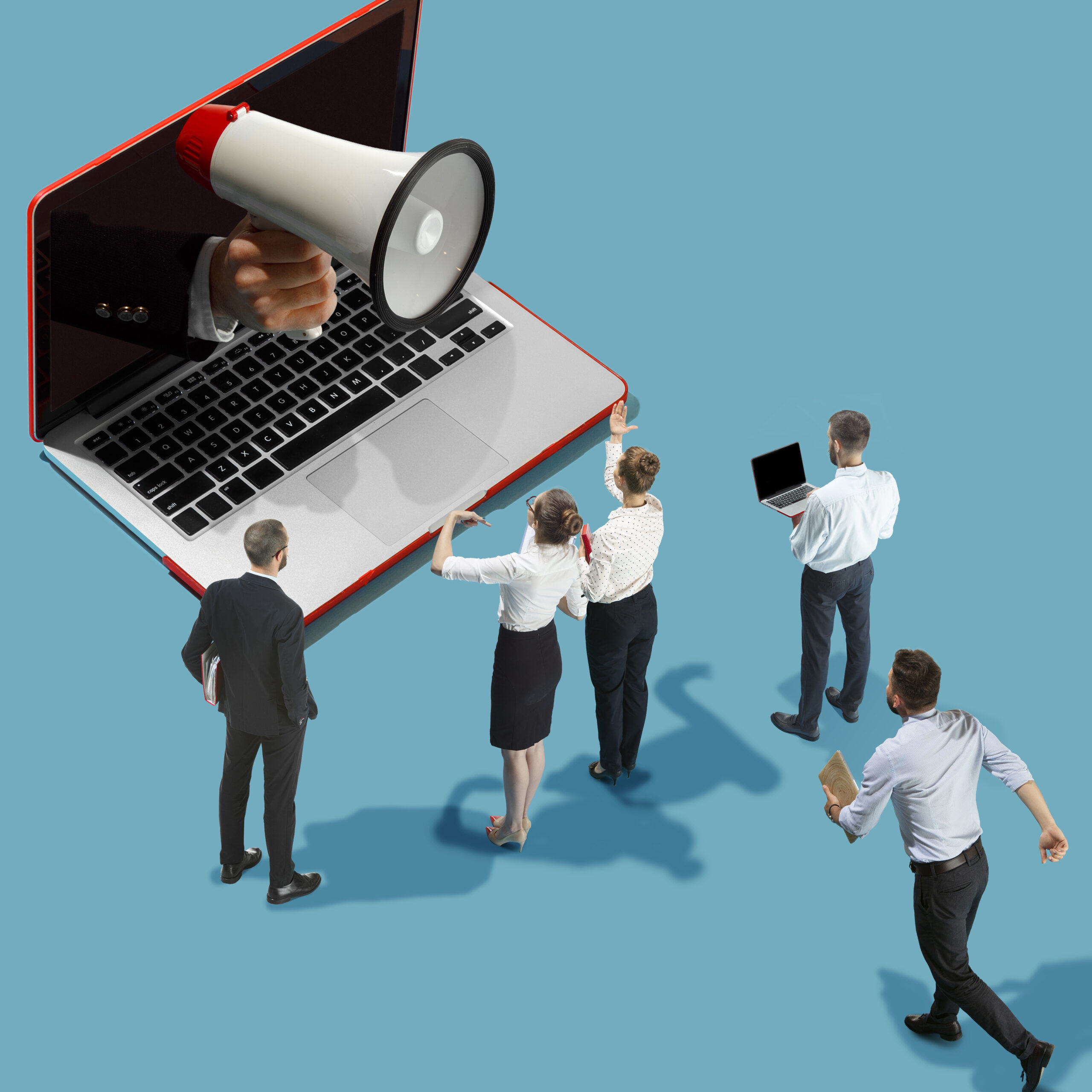 Des employés miniatures en tenue professionnelle observent un grand ordinateur portable dont l’écran laisse sortir une main tenant un mégaphone, sur fond bleu uni.