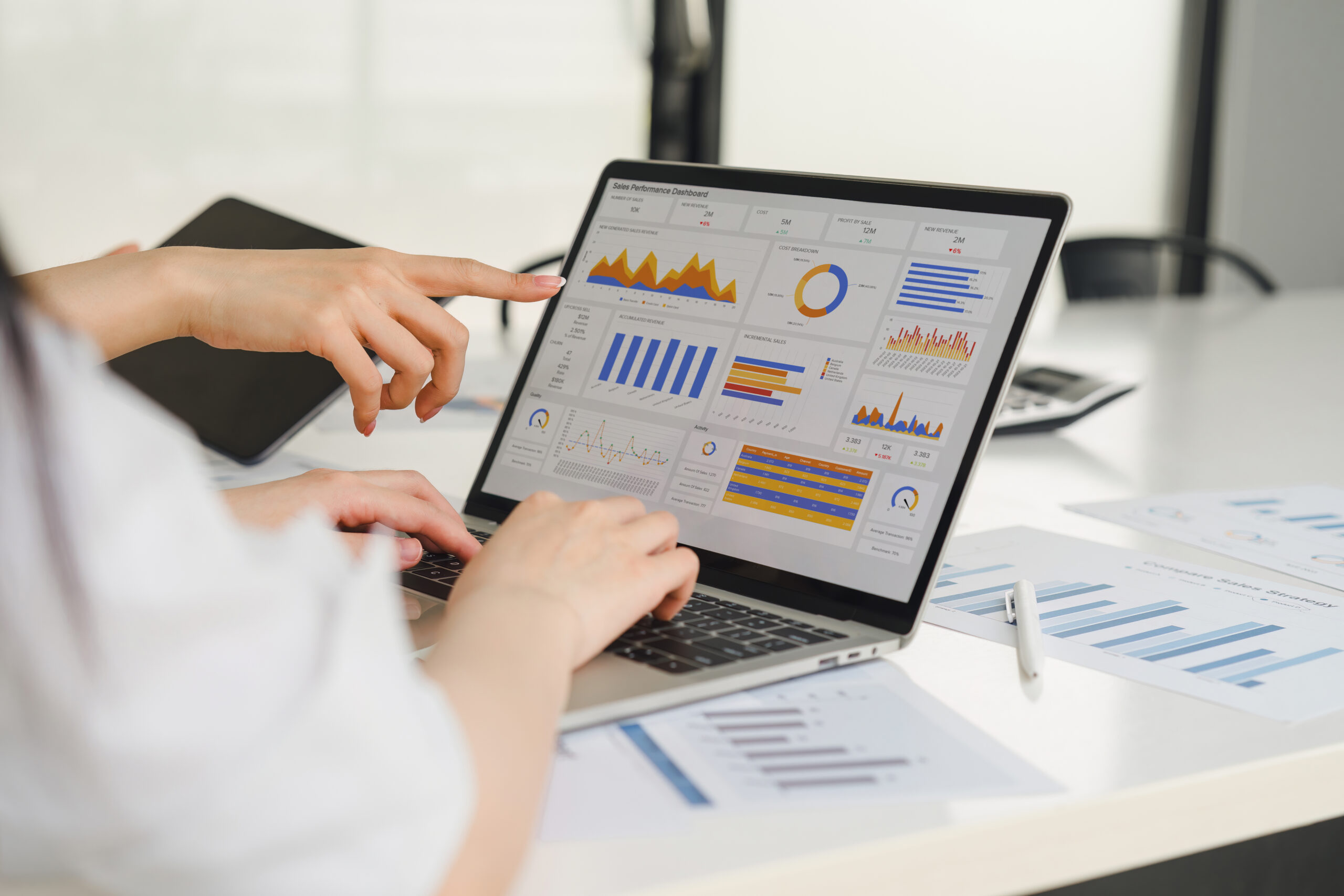 Deux personnes analysent un tableau de bord interactif sur un ordinateur portable, affichant des graphiques de performance commerciale et des indicateurs de données.